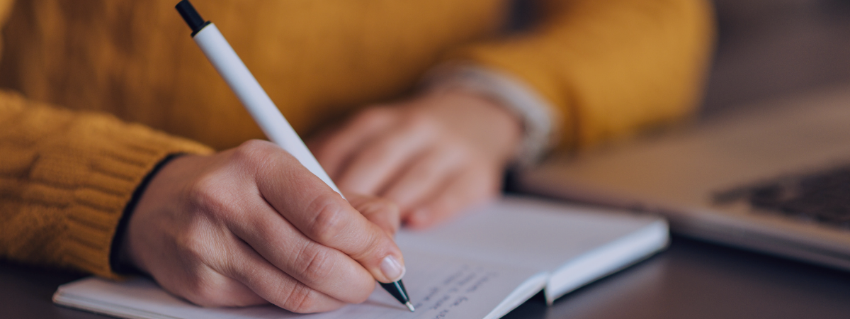 A person sits at a desk writing in a journal.