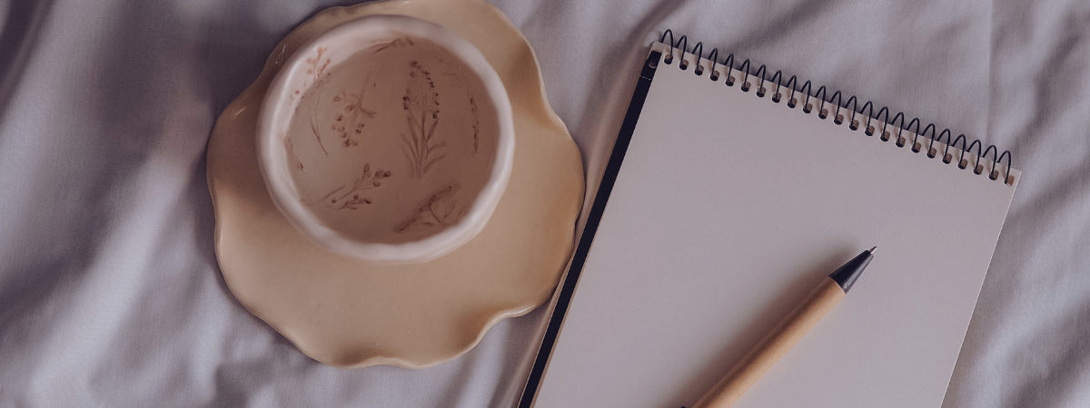 A mug, notebook, and pen sit on top of a bed.