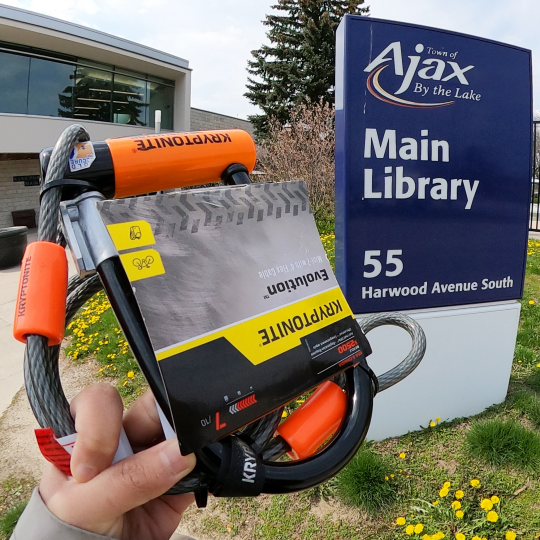 A hand holding up a bike lock in front of Main Branch