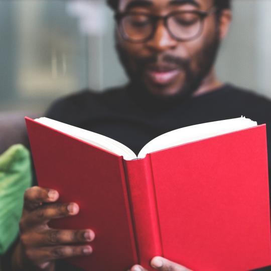 Man reading book with bright red cover.