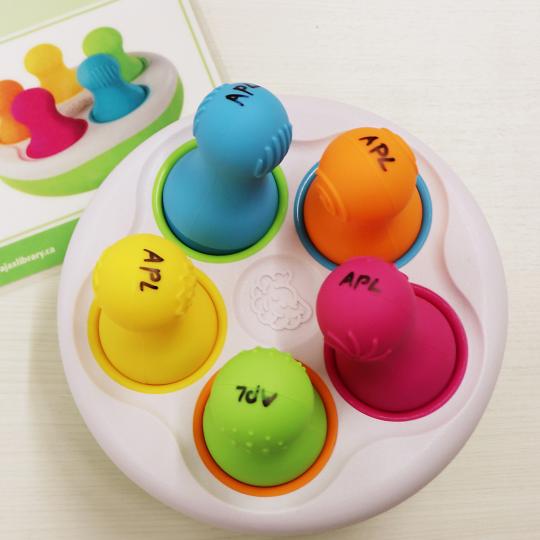 Colourful Spinny Pins sit in a white container on a white table at Audley Branch.