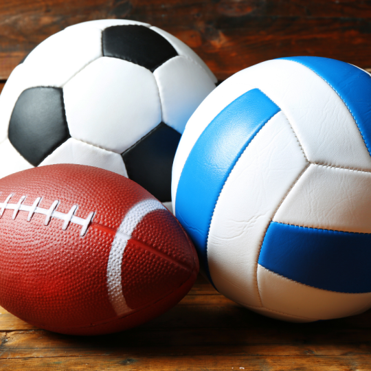 A soccer ball, football, and volleyball. 