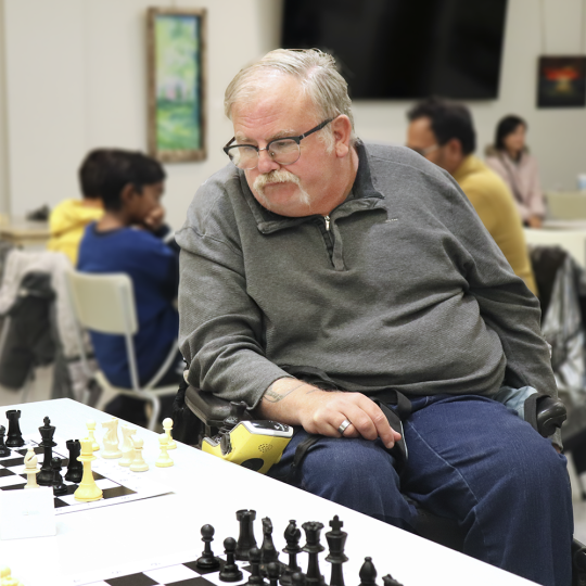 A person with glasses and short gray hair plays chess in the Rotary Room at Main Branch.