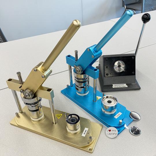 Two button makers, one gold, and one blue, plus a circle cutter. 